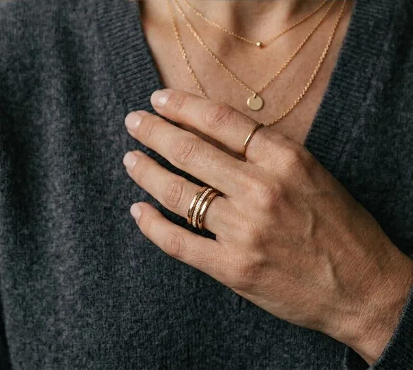A hand and neckline wearing layered gold jewelry